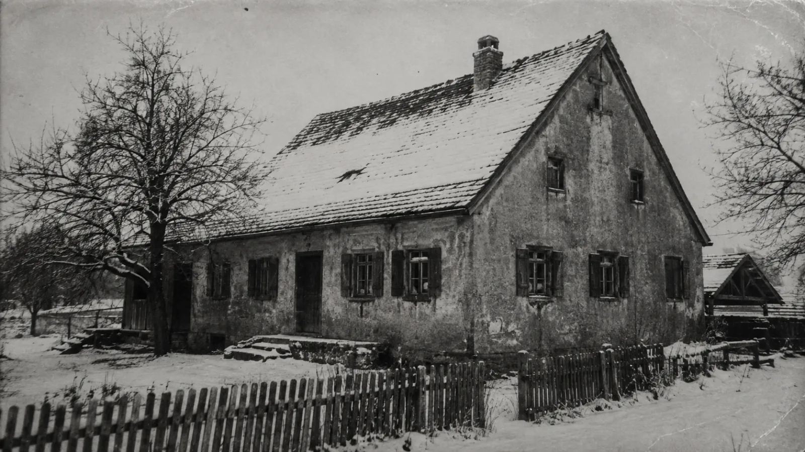 A weathered, black-and-white style photograph of an old German farmhouse exterior in winter