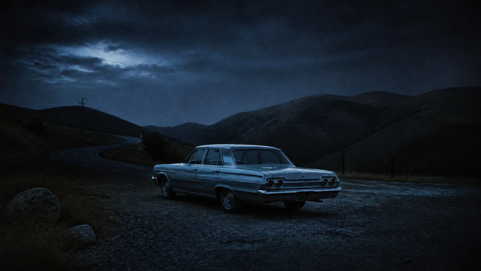 1960s car parked alone on a remote gravel turnout at night with headlights off, surrounded by dark hills