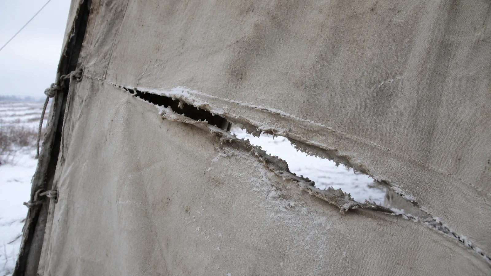 Close-up illustration of a torn canvas tent wall with a long slash cut through the fabric from the inside